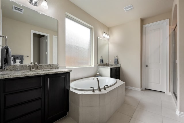 bathroom with tile patterned flooring, vanity, and a relaxing tiled tub