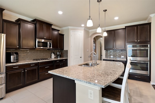 kitchen with a center island with sink, sink, light stone countertops, tasteful backsplash, and stainless steel appliances