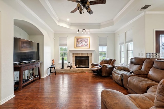 living room with dark wood-type flooring, ornamental molding, a tray ceiling, and a tile fireplace