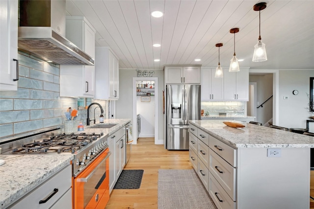 kitchen with stainless steel appliances, white cabinetry, a kitchen island, wall chimney range hood, and a sink