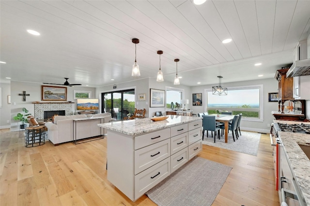 kitchen featuring stainless steel range, a kitchen island, light stone countertops, white cabinetry, and pendant lighting