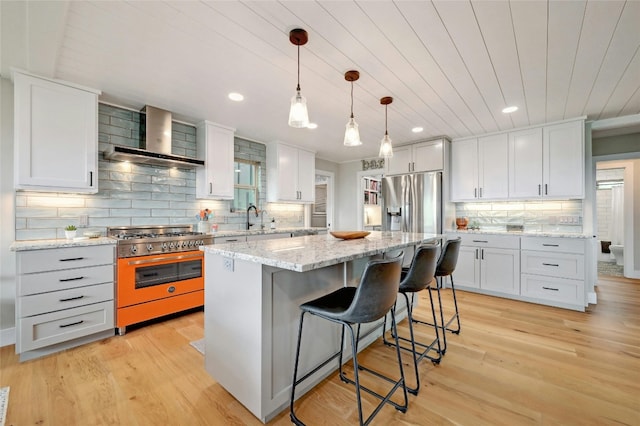 kitchen with appliances with stainless steel finishes, hanging light fixtures, a kitchen island, and wall chimney range hood