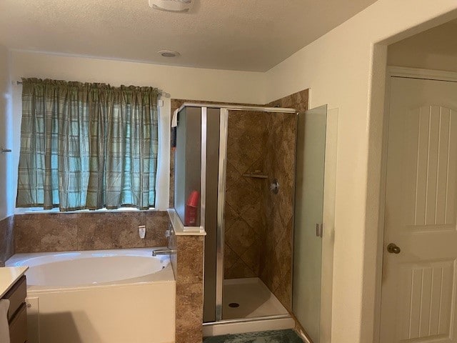 bathroom with a textured ceiling, vanity, and shower with separate bathtub