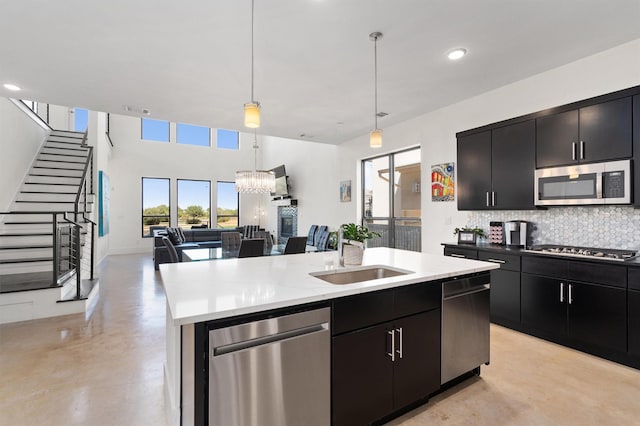 kitchen with sink, hanging light fixtures, appliances with stainless steel finishes, an island with sink, and decorative backsplash