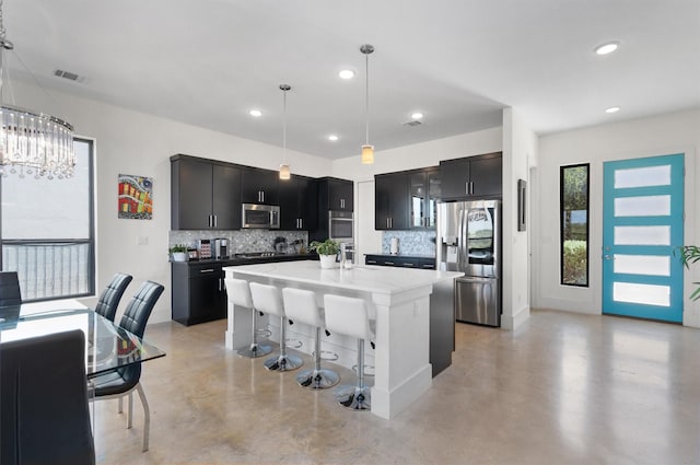 kitchen with a kitchen bar, a center island with sink, pendant lighting, stainless steel appliances, and backsplash