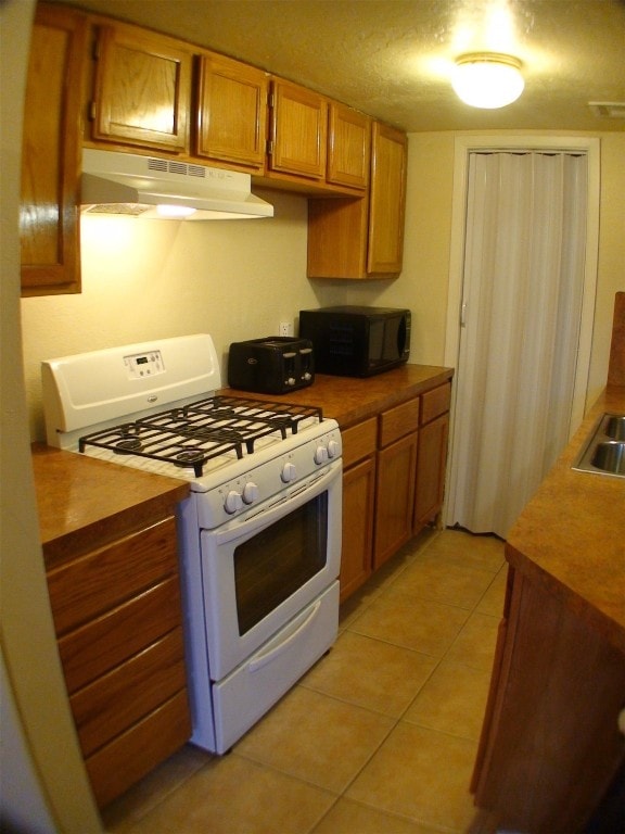 kitchen with white range with gas stovetop, a textured ceiling, and light tile patterned floors