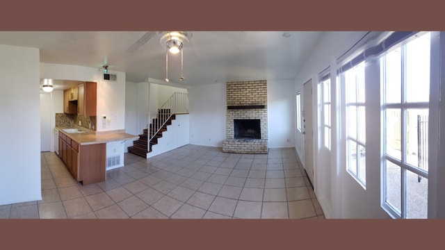 kitchen featuring backsplash, sink, light tile patterned floors, a fireplace, and kitchen peninsula