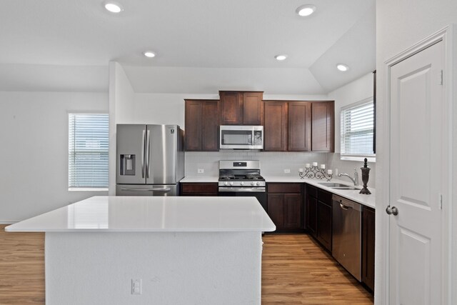 kitchen with a center island, tasteful backsplash, light hardwood / wood-style flooring, lofted ceiling, and appliances with stainless steel finishes