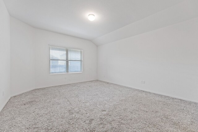 carpeted spare room with vaulted ceiling