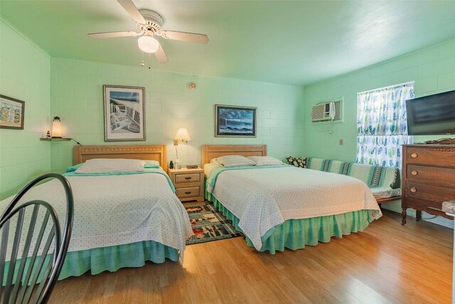 bedroom with light hardwood / wood-style flooring, ceiling fan, and an AC wall unit