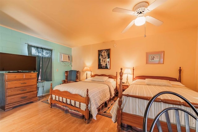 bedroom with light wood-type flooring, a wall unit AC, and ceiling fan