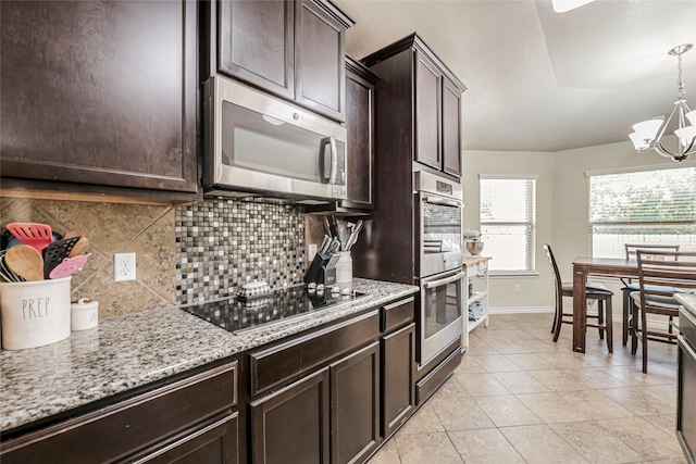 kitchen featuring appliances with stainless steel finishes, tasteful backsplash, a notable chandelier, light stone countertops, and dark brown cabinets