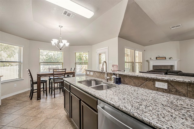 kitchen featuring pendant lighting, a fireplace, dishwasher, sink, and light stone counters