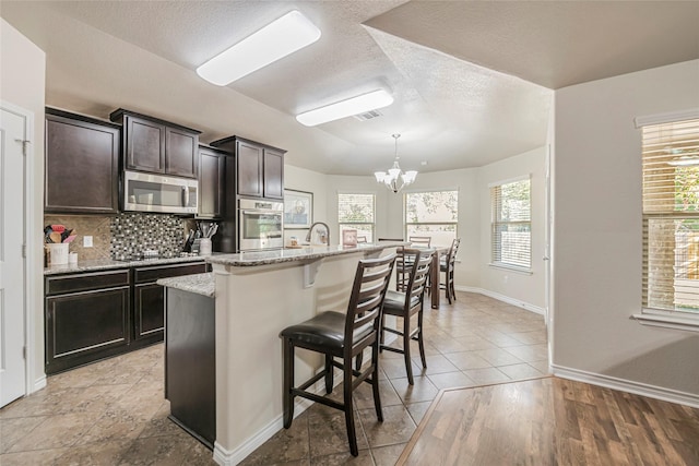 kitchen with hanging light fixtures, a kitchen breakfast bar, stainless steel appliances, a kitchen island with sink, and decorative backsplash