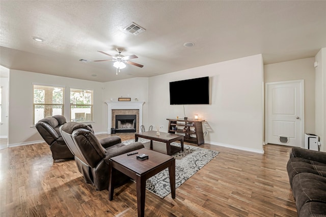 living room featuring a tiled fireplace, ceiling fan, a textured ceiling, and light hardwood / wood-style floors