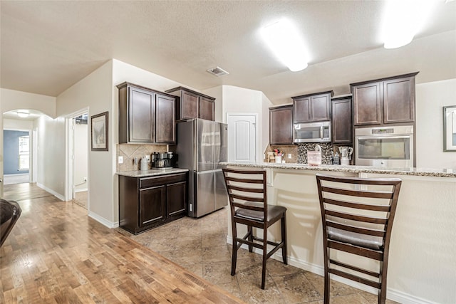 kitchen featuring dark brown cabinetry, decorative backsplash, stainless steel appliances, and a kitchen bar