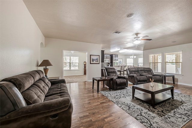 living room featuring hardwood / wood-style flooring, a wealth of natural light, a textured ceiling, and ceiling fan with notable chandelier