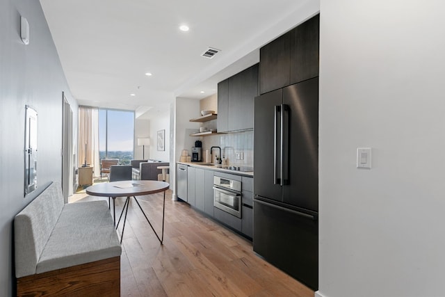 kitchen with decorative backsplash, expansive windows, stainless steel appliances, and light hardwood / wood-style floors