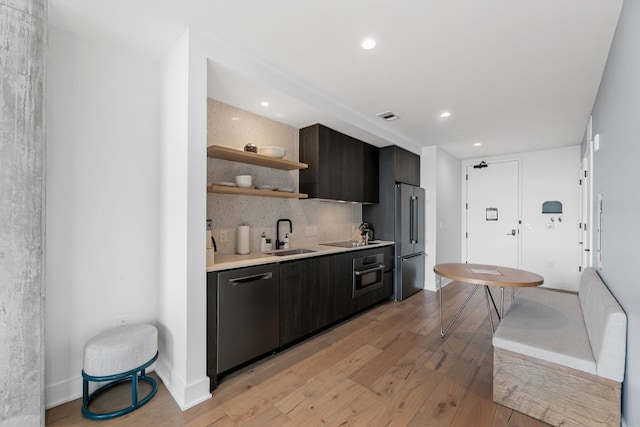 kitchen featuring sink, light wood-type flooring, appliances with stainless steel finishes, tasteful backsplash, and dark brown cabinetry