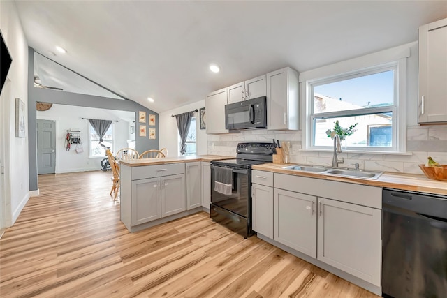 kitchen with black appliances, plenty of natural light, kitchen peninsula, and vaulted ceiling