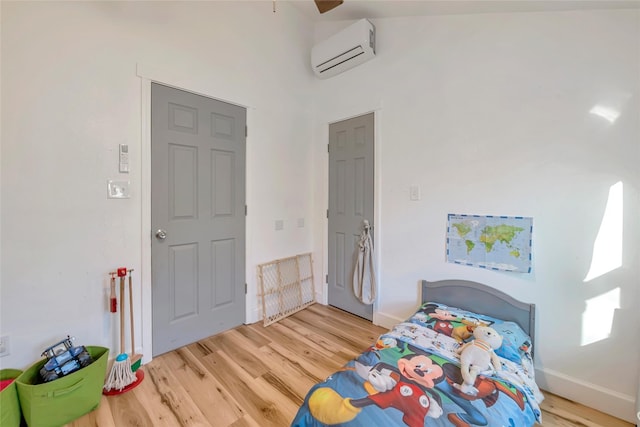 bedroom with a towering ceiling, light wood-type flooring, an AC wall unit, and ceiling fan