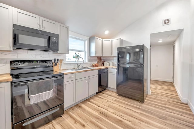 kitchen with butcher block counters, sink, tasteful backsplash, light hardwood / wood-style flooring, and black appliances