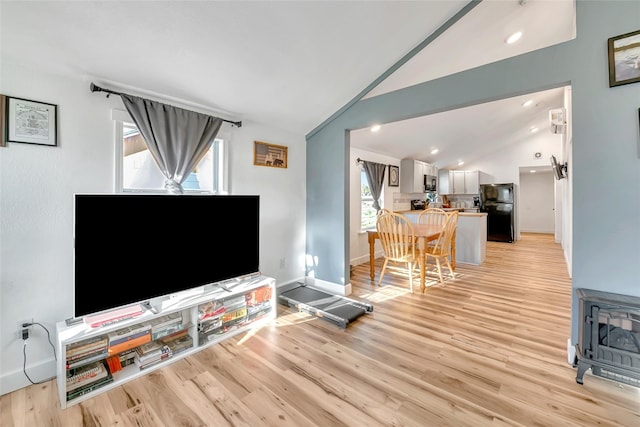 living room featuring a wood stove, light hardwood / wood-style floors, and vaulted ceiling