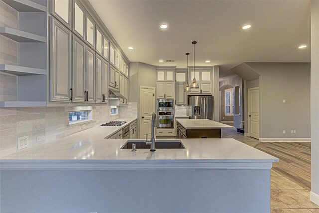 kitchen with light hardwood / wood-style flooring, kitchen peninsula, decorative light fixtures, a kitchen island, and appliances with stainless steel finishes