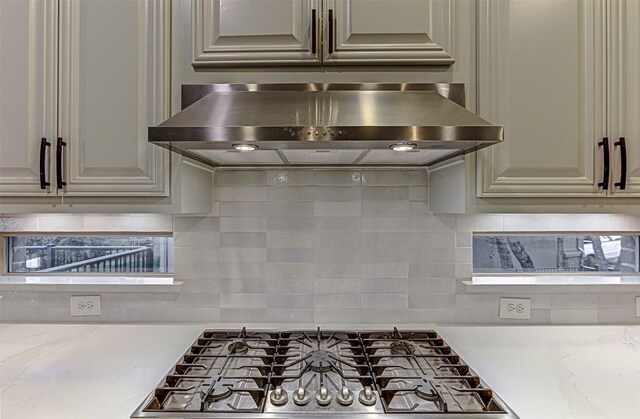 kitchen with ventilation hood, decorative backsplash, and light stone countertops