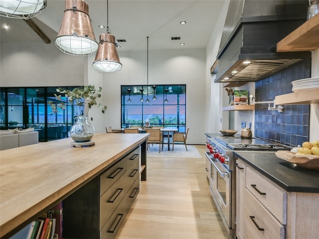 kitchen with tasteful backsplash, high end stove, light hardwood / wood-style floors, pendant lighting, and custom exhaust hood