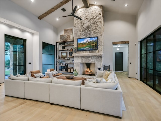 living room with beamed ceiling, light hardwood / wood-style floors, a stone fireplace, and high vaulted ceiling