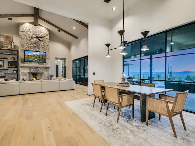 dining area featuring hardwood / wood-style floors, beam ceiling, high vaulted ceiling, and a large fireplace