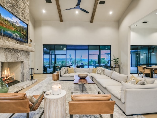 living room featuring a fireplace, beam ceiling, light hardwood / wood-style floors, and a high ceiling