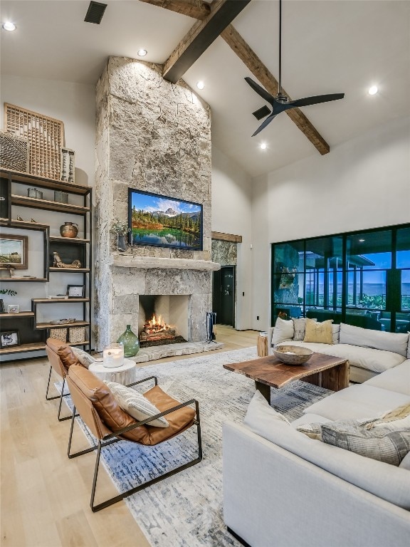 living room featuring high vaulted ceiling, ceiling fan, light wood-type flooring, a fireplace, and beam ceiling