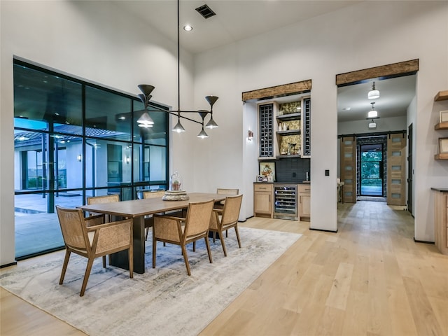 dining room with bar area, a towering ceiling, beverage cooler, and light wood-type flooring