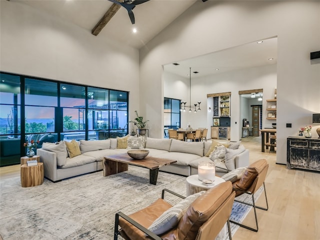 living room featuring beam ceiling, ceiling fan with notable chandelier, light hardwood / wood-style floors, and high vaulted ceiling