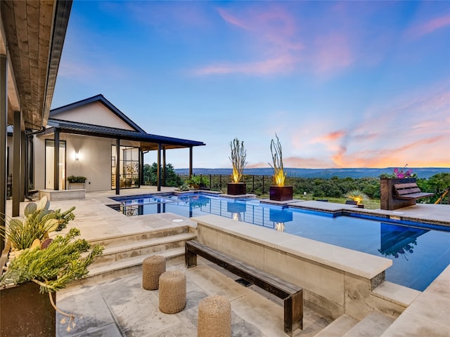 pool at dusk featuring a patio area and a hot tub