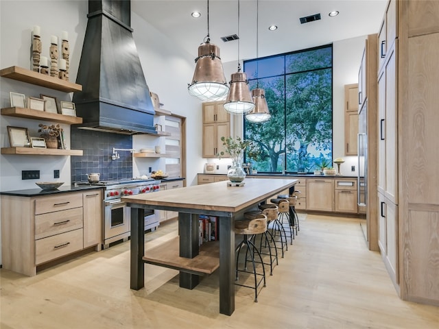 kitchen with light wood-type flooring, luxury range, custom range hood, light brown cabinets, and decorative light fixtures