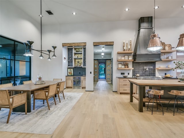 kitchen featuring beverage cooler, premium range hood, light hardwood / wood-style floors, decorative light fixtures, and decorative backsplash