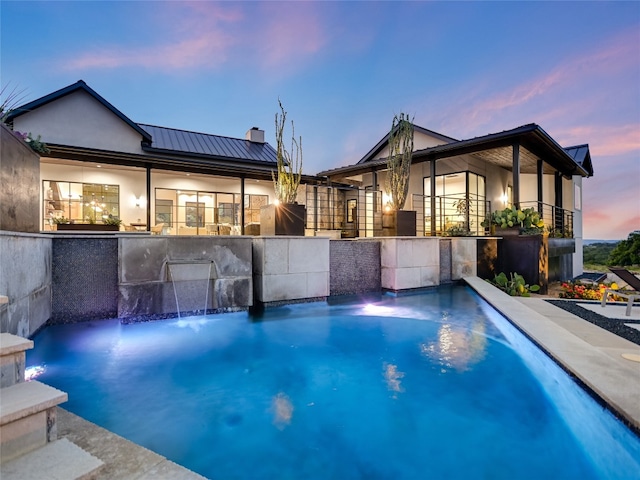 pool at dusk featuring pool water feature