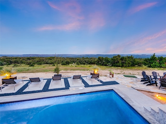 pool at dusk featuring an outdoor fire pit and a patio