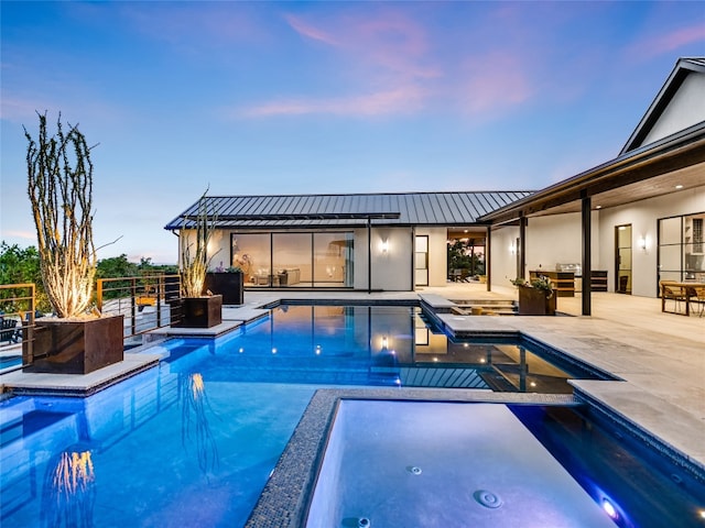 pool at dusk featuring an in ground hot tub and a patio