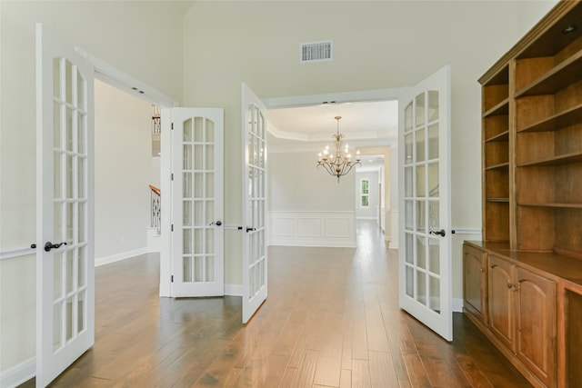 hall with a notable chandelier, wood-type flooring, and french doors