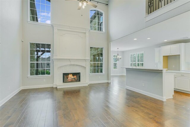 unfurnished living room featuring a ceiling fan, a premium fireplace, a towering ceiling, plenty of natural light, and wood finished floors