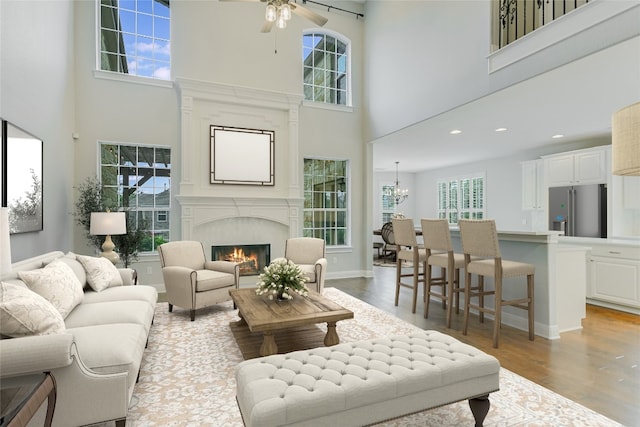 living room featuring ceiling fan with notable chandelier, a high ceiling, a wealth of natural light, and light hardwood / wood-style flooring