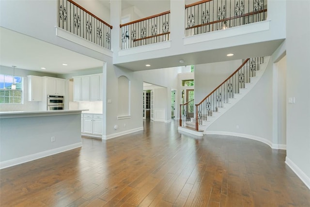 unfurnished living room with dark wood-style flooring, stairway, a high ceiling, and baseboards