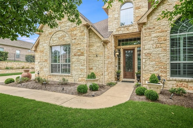 view of exterior entry with stone siding, a shingled roof, and a lawn