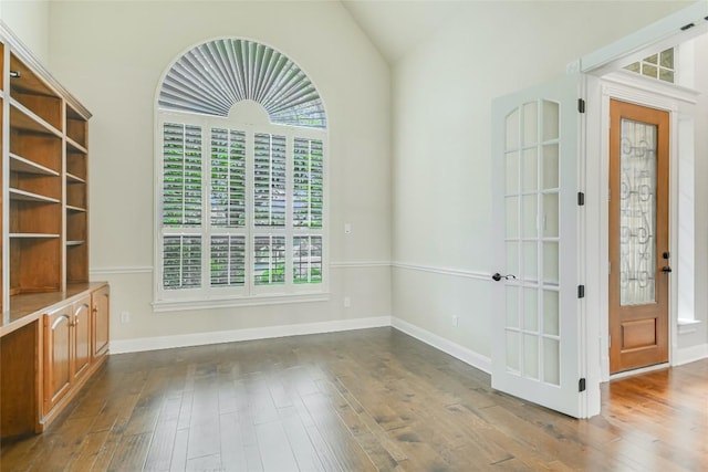 unfurnished dining area with healthy amount of natural light, dark wood-type flooring, vaulted ceiling, and baseboards