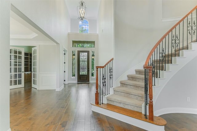 foyer entrance featuring wood finished floors, a towering ceiling, stairway, a chandelier, and crown molding
