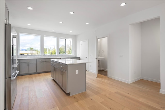 kitchen featuring stainless steel refrigerator, sink, light hardwood / wood-style flooring, gray cabinets, and a kitchen island